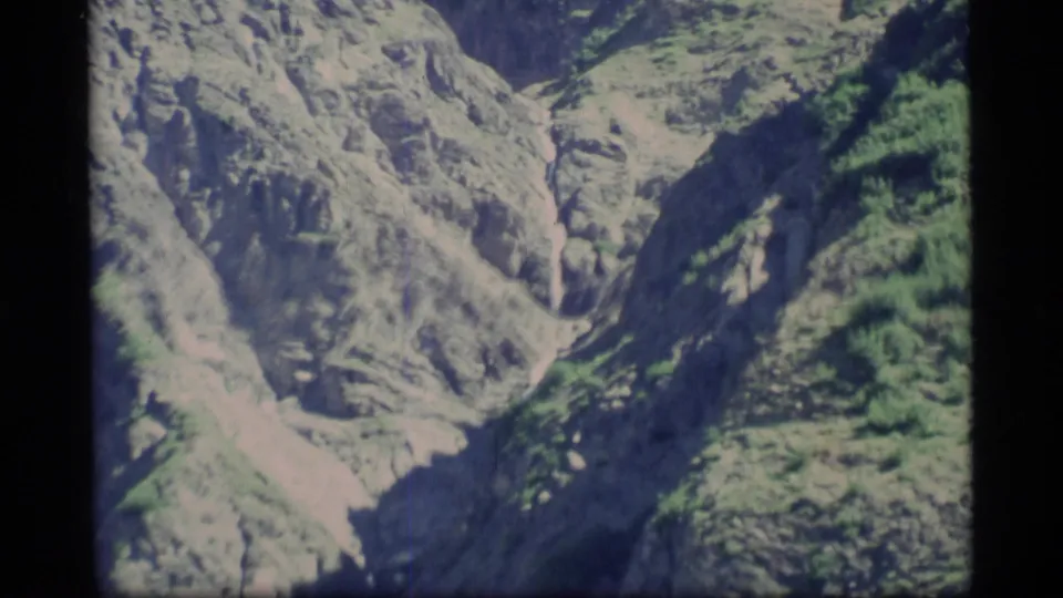 1977 Alaska 8mm frame of a rugged canyon, green mountain sides, and a pale winding watercourse below.