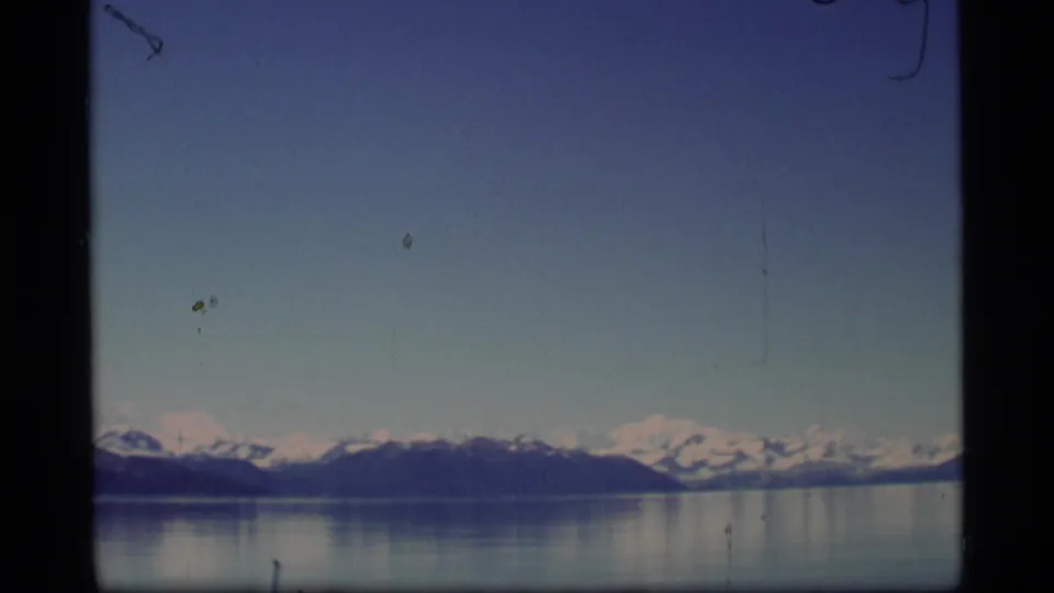 1977 Alaska 8mm frame showing open water, a distant snowy mountain range, blue sky, and film dust marks.