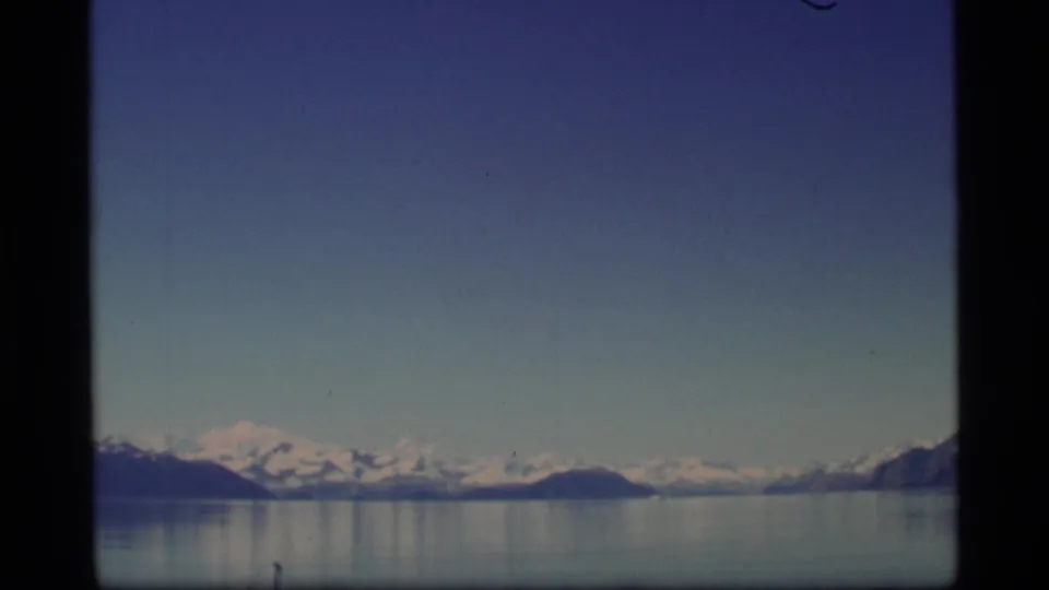 Alaska landscape on 8mm film with snow-capped peaks, still water, and a broad blue sky framed by the scan area.