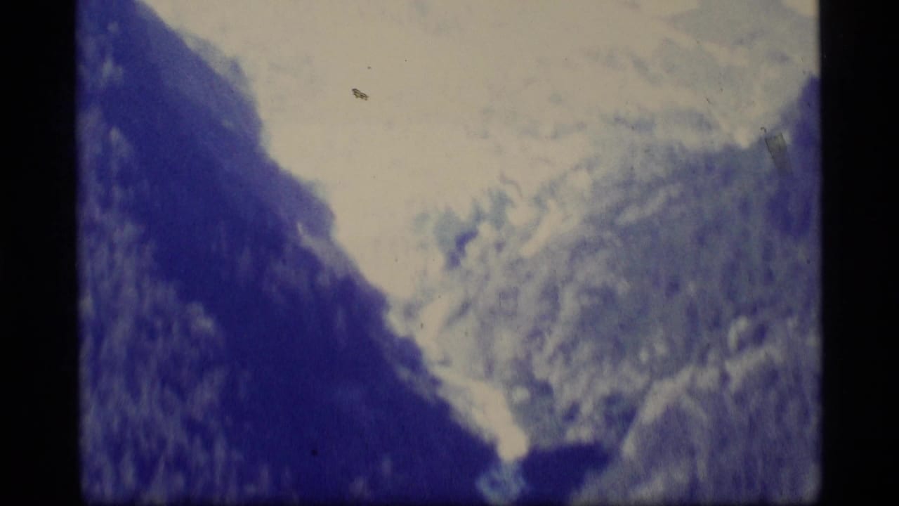 1977 Alaska 8mm frame showing a distant mountainous or valley landscape with soft focus, grain, and strong blue vintage color shift.