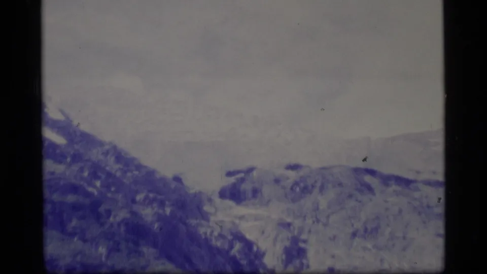 1977 Alaska 8mm frame with distant snowy mountain ridges under a pale overcast sky and visible film border.