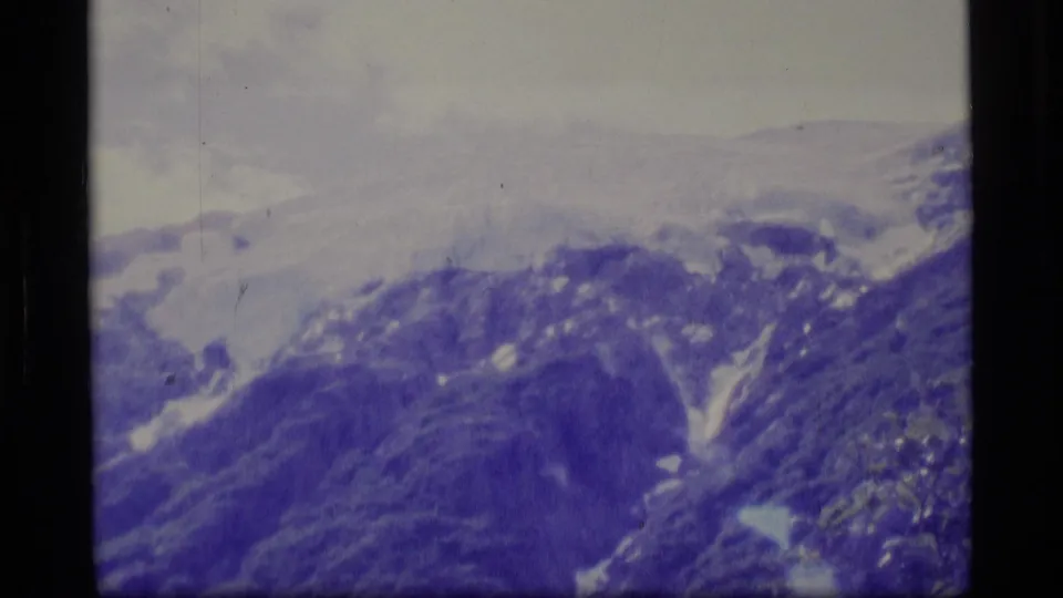1977 Alaska 8mm mountain view with snow patches, distant ridges, pale sky, and visible color shift from the film scan.