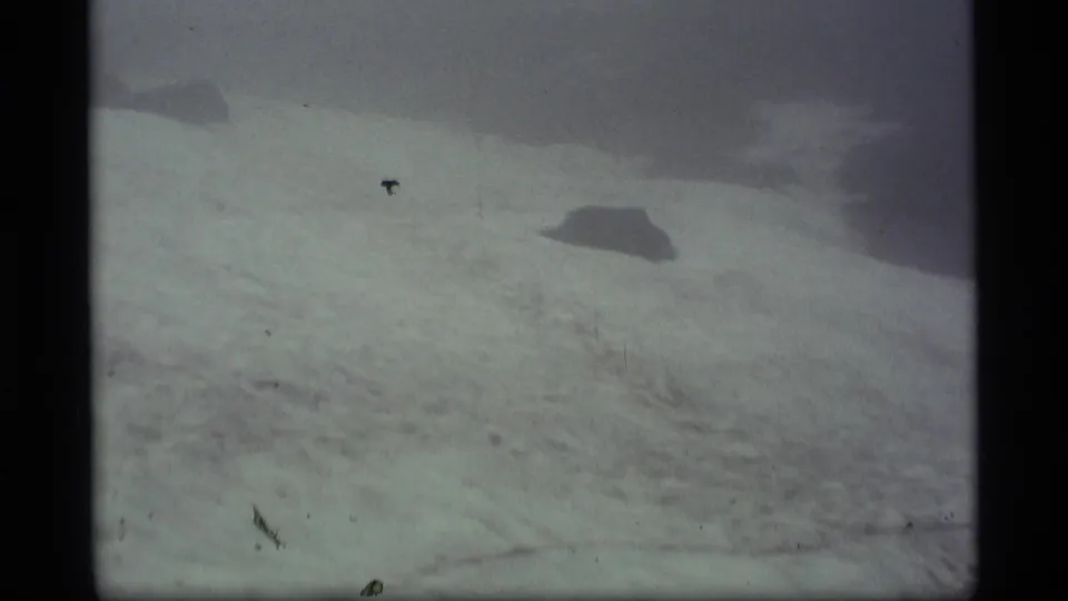 1977 Alaska 8mm frame showing a pale snow-covered slope or ice field with dark distant landforms and grainy exposure.