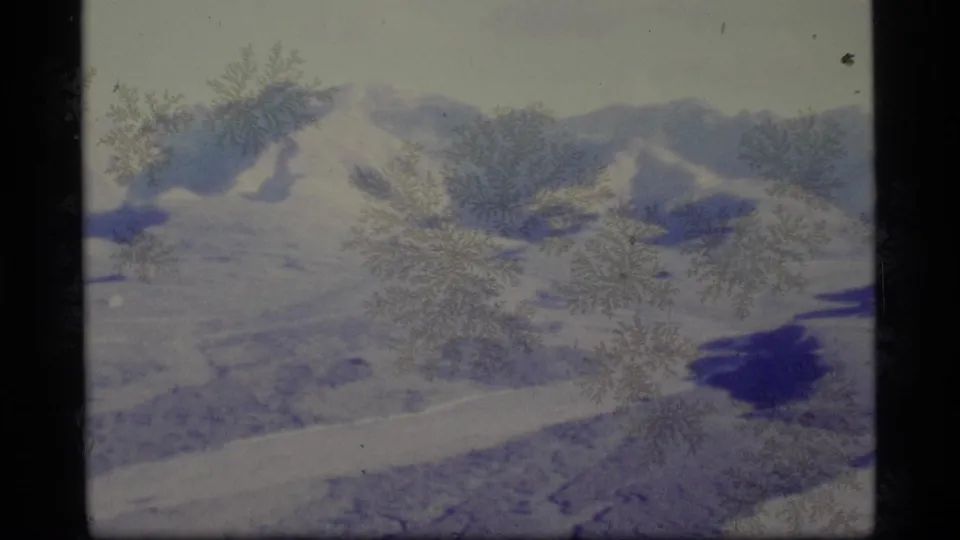 A broad Alaska mountain view shows snowfields, blue shadows, and frost-like film artifacts in 1977 8mm footage.