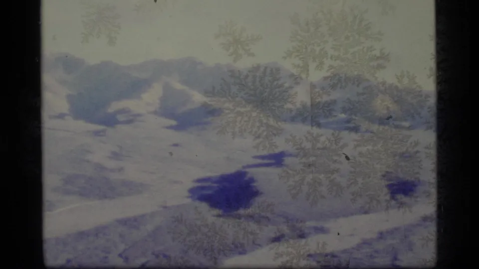 The 1977 Alaska home-movie clip ends on a snowy mountain panorama with dark shadow patches and aged film texture.