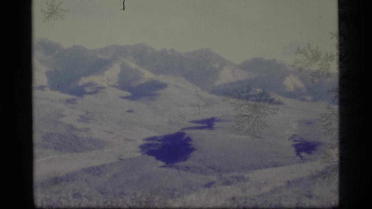 1977 Alaska 8mm frame showing snowy distant mountains and an open valley with visible grain, color shift, and frame border.