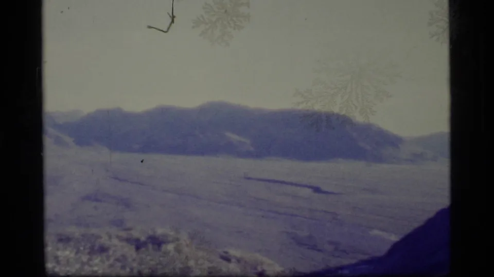 1977 Alaska 8mm frame with a broad snowy valley, dark mountain ridge, pale sky, and softened home-movie exposure.