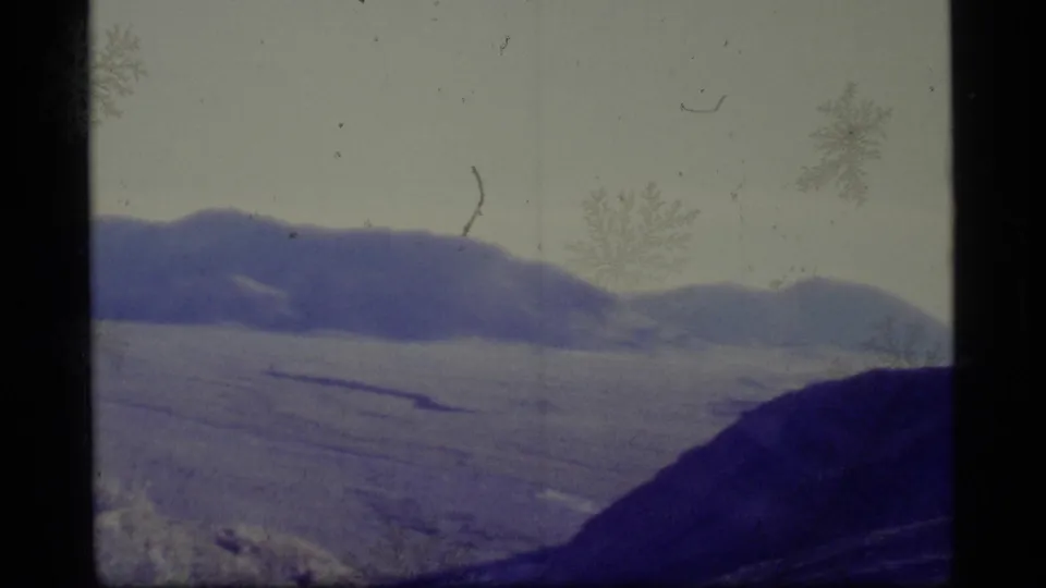 1977 Alaska 8mm frame showing a snow-covered valley, distant mountain ridge, darker foreground slope, and aged film texture.