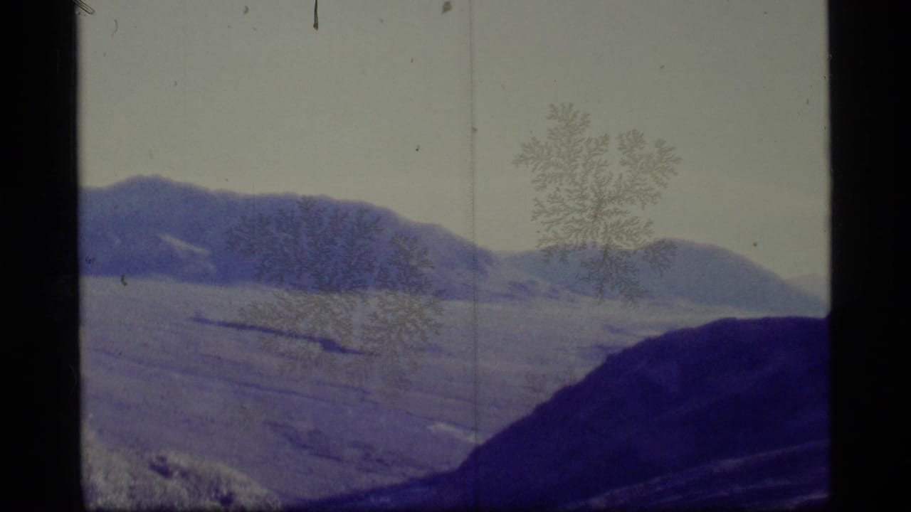1977 8mm Alaska travel footage shows distant mountains and a dark foreground ridge under a pale overcast sky.