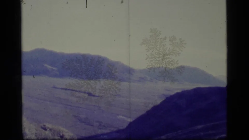 1977 8mm Alaska travel footage shows distant mountains and a dark foreground ridge under a pale overcast sky.