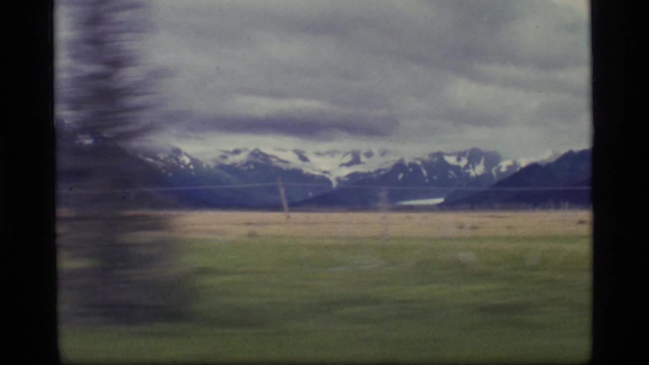 1977 Alaska 8mm frame showing snow-capped mountains across a broad field, filmed with soft motion blur from a moving viewpoint.