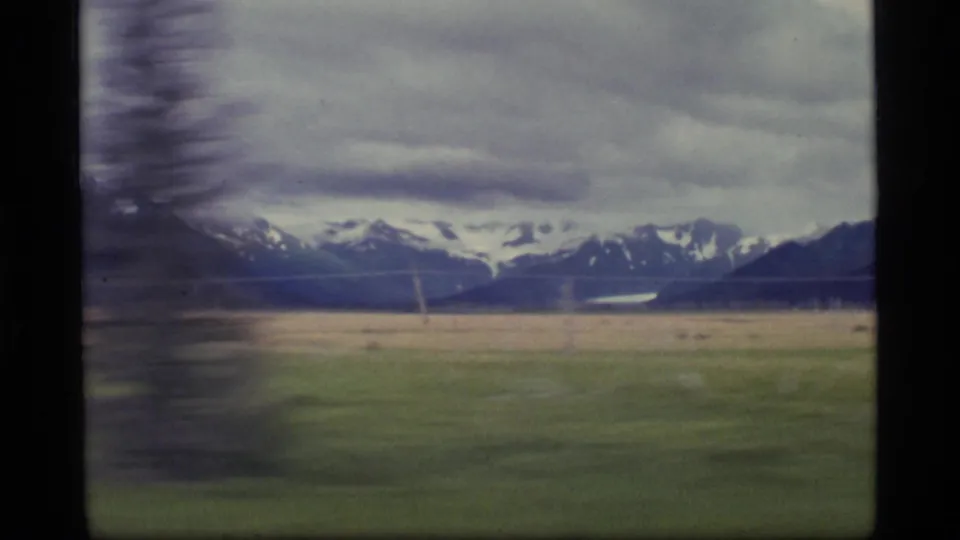 1977 Alaska 8mm frame showing snow-capped mountains across a broad field, filmed with soft motion blur from a moving viewpoint.