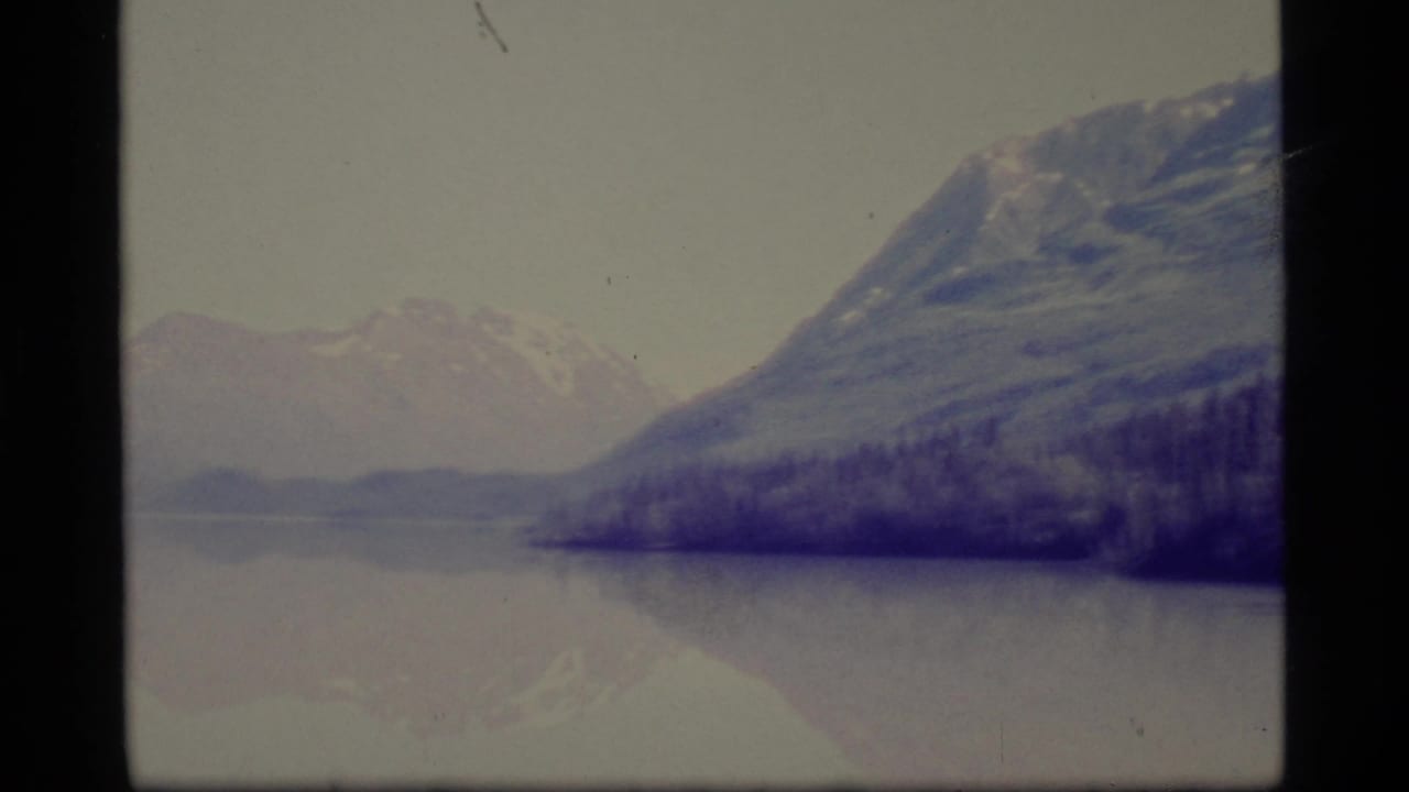 Snowy mountains and forested slopes reflected in a calm lake.