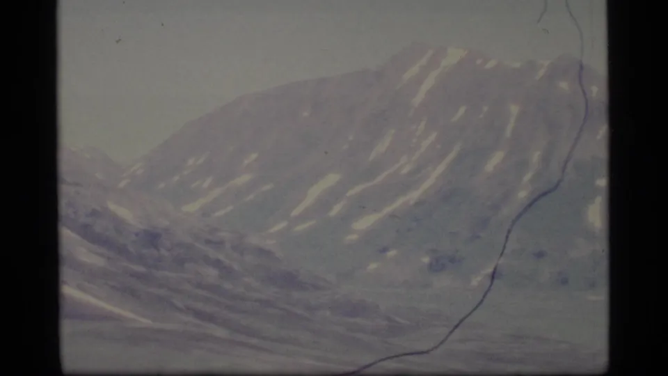 1977 Alaska 8mm frame showing a hazy mountain peak with snow patches and muted blue-gray tones.