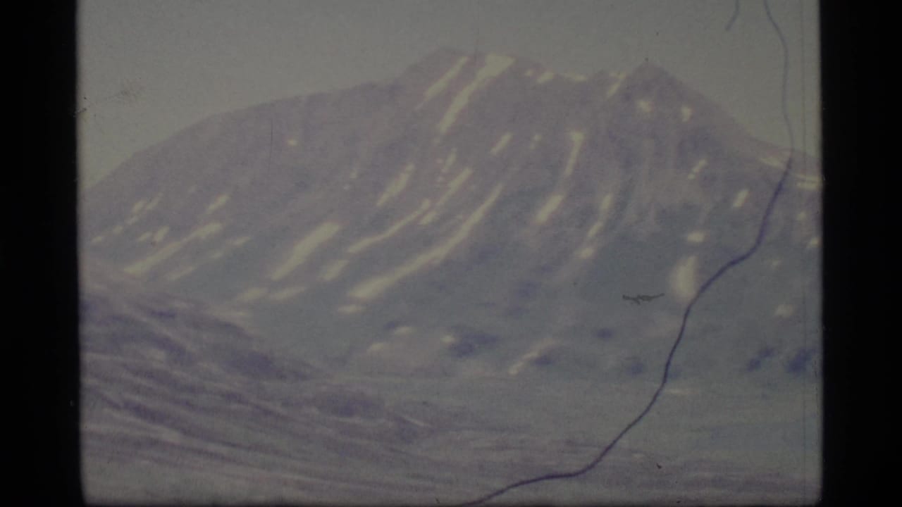 Snow-streaked mountain ridge beneath a pale sky with visible film scratches and gate edges.