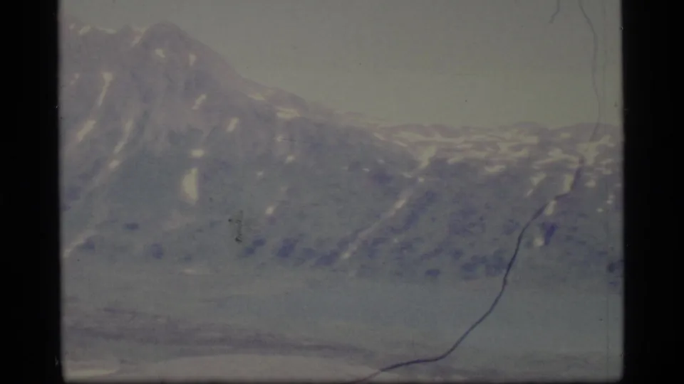 1977 Alaska 8mm frame showing a sloped mountain edge and lower snow-dusted ridges in faded home-movie color.