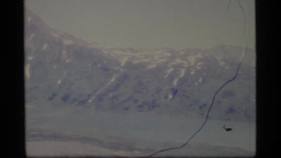 1977 Alaska 8mm frame of distant snow-marked ridges under a pale sky, with visible film scratches and dust specks.