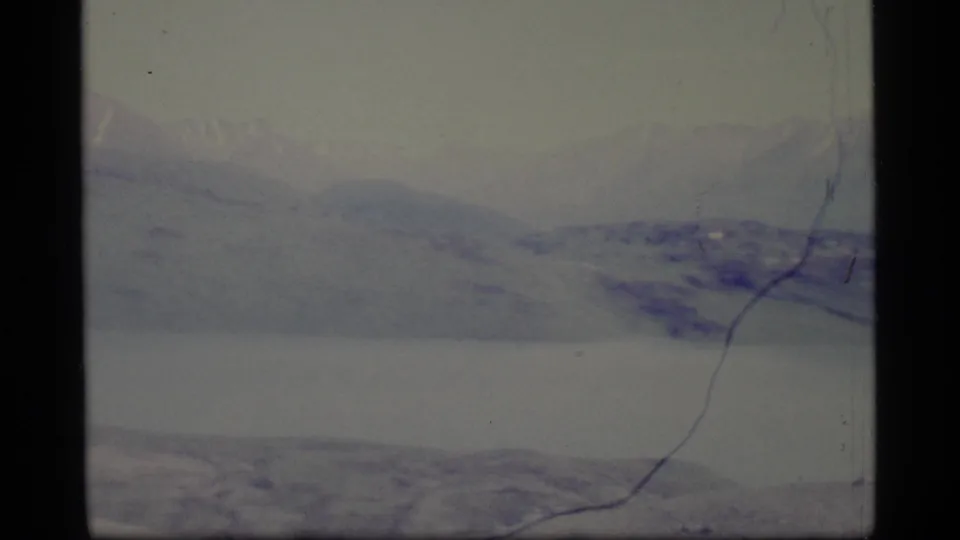 1977 Alaska 8mm frame with layered distant peaks, lake surface, and a strong vertical scratch near the right side.