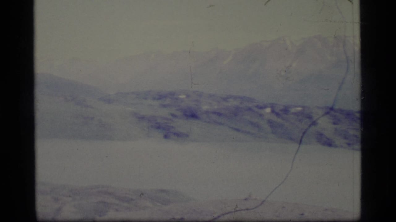 1977 Alaska 8mm frame showing a broad snowy expanse and hazy mountain range with visible film scratches and dark frame edge.