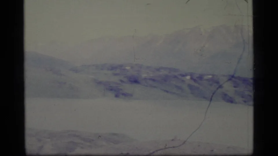 1977 Alaska 8mm frame showing a broad snowy expanse and hazy mountain range with visible film scratches and dark frame edge.