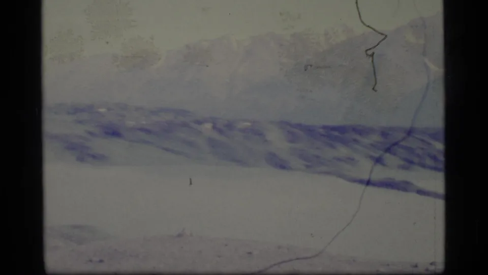 1977 Alaska home-movie frame with a snow-covered foreground, distant mountain ridge, pale haze, and visible 8mm frame borders.