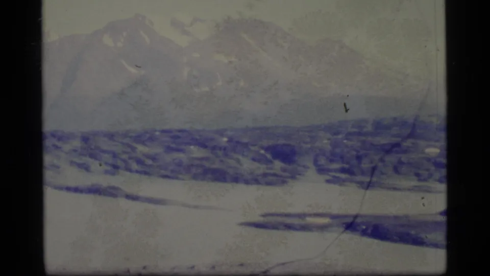 1977 Alaska 8mm frame with distant snowy peaks, a wide frozen foreground, dark frame borders, and visible film wear.