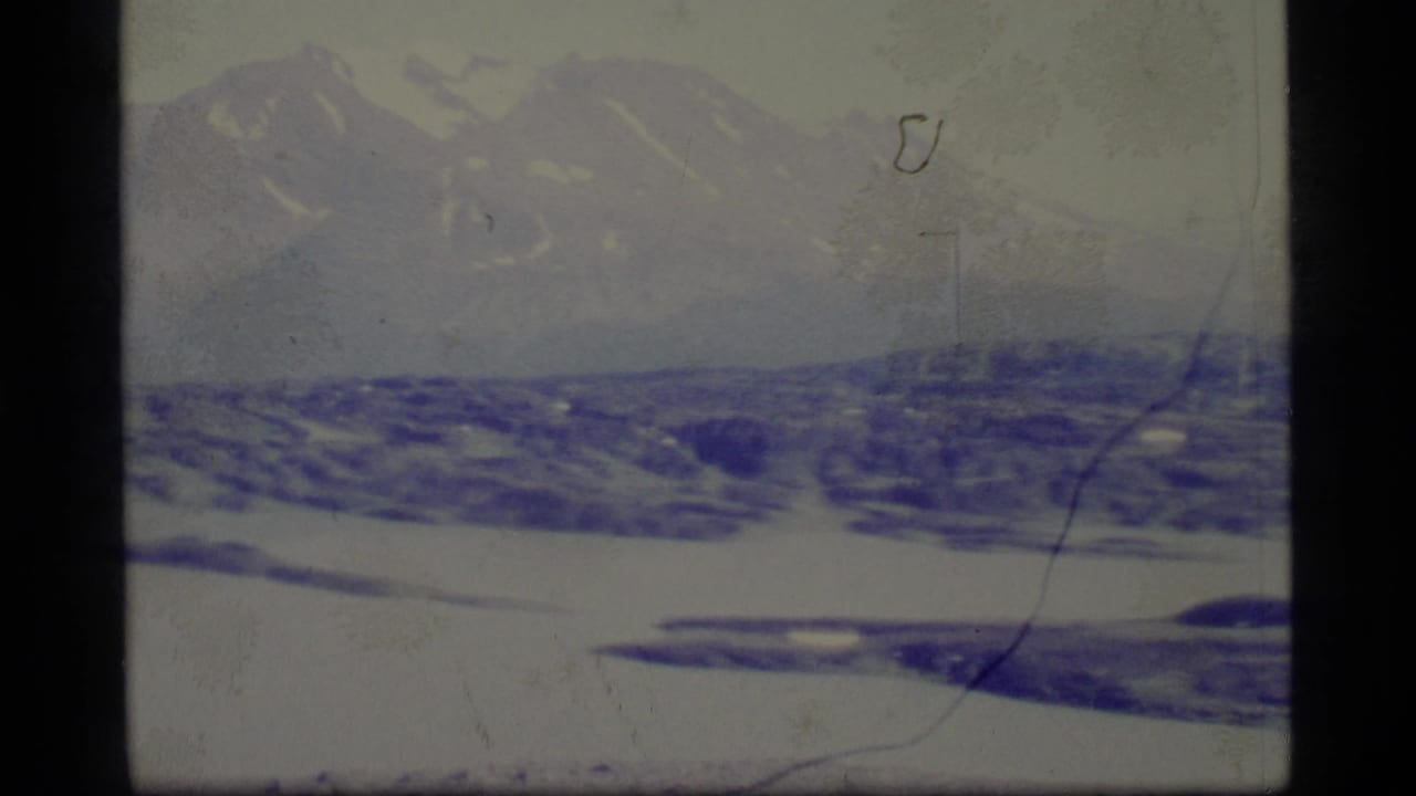 1977 Alaska 8mm frame showing snow-covered hills, distant mountains, pale winter sky, and visible film wear.