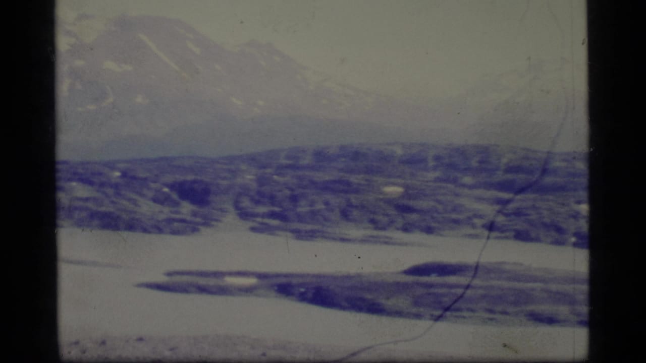 Distant mountain range above dark snowy hills and a white horizontal snow or ice band.