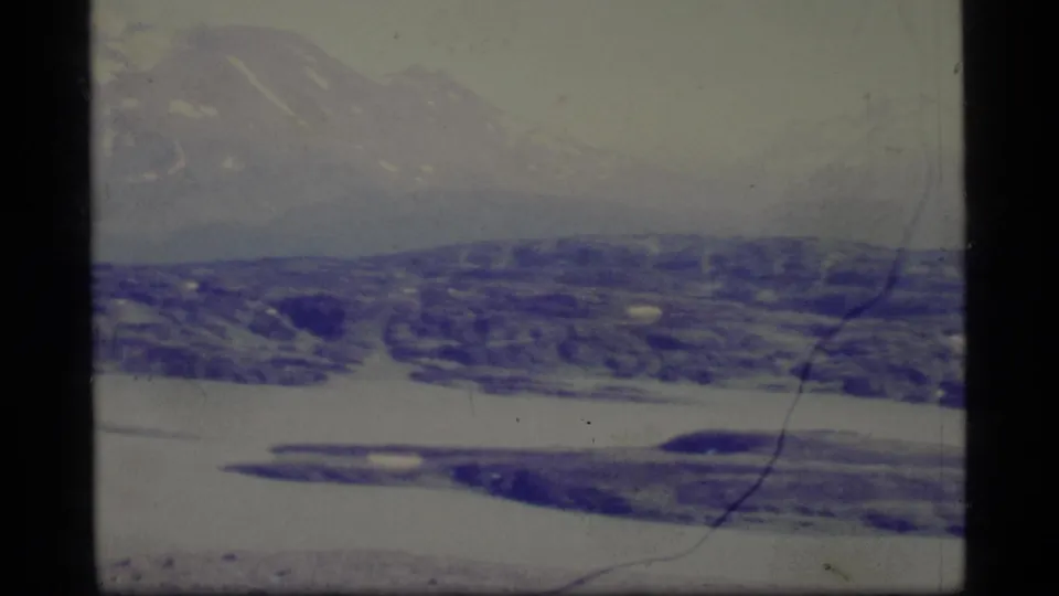 1977 Alaska winter landscape with mountains, rolling hills, pale sky, and blue-purple 8mm color fading.