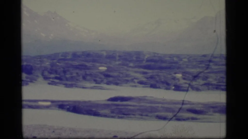 Faded 1977 Alaska 8mm frame with soft mountains, dark snowy hills, and broad white snow or ice across the middle.