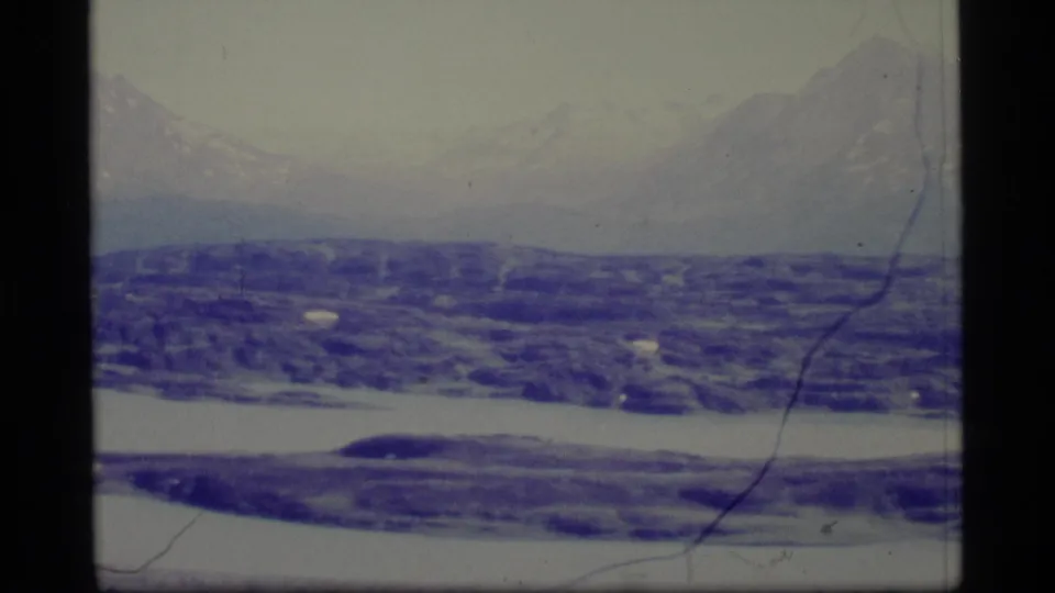1977 Alaska 8mm view of remote winter hills, faint mountain peaks, pale sky, and scratched film surface.