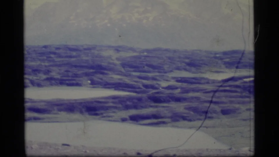 1977 Alaska 8mm frame emphasizing textured icy ground or water, with faint mountains above and pronounced aged-film marks.