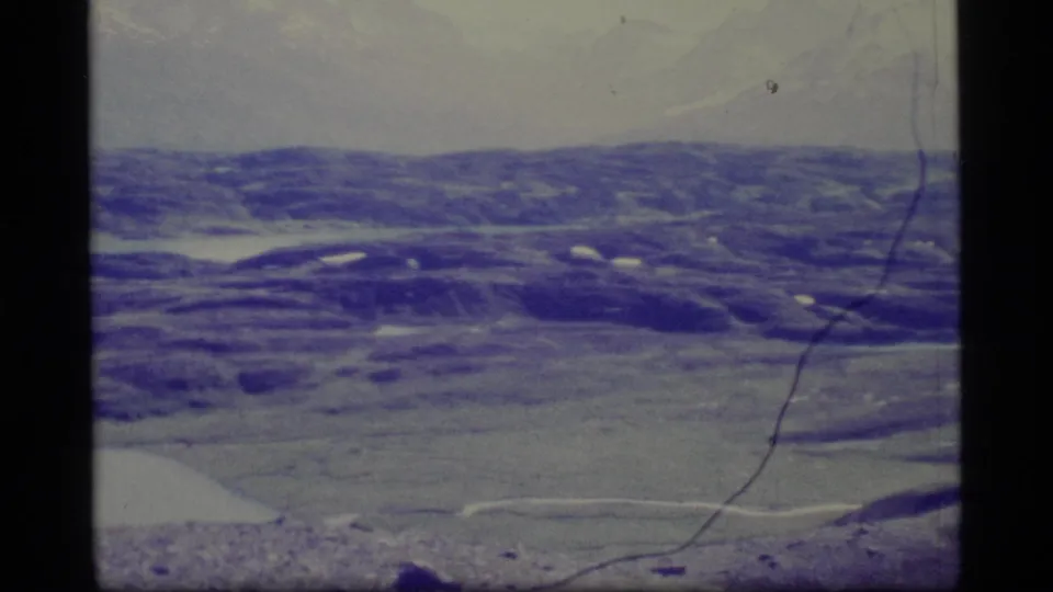Aged 8mm frame of an Alaskan valley area from above, with snow patches, soft focus, and blue-purple fading.