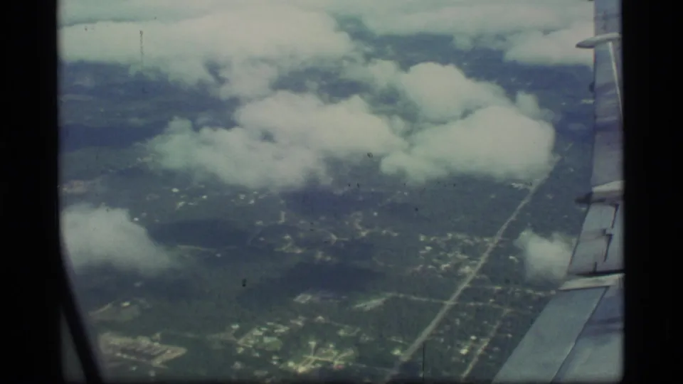 1977 Alaska in-flight view with the aircraft wing at right, low clouds, visible roads, and mottled landscape below.
