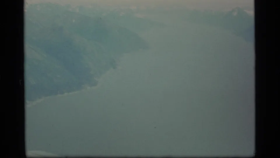 1977 8mm Alaska aerial view with pale water or atmospheric haze and faint coast or mountain slopes along the upper frame.