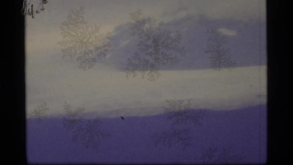 1977 Alaska 8mm frame of a distant snow-covered ridge beneath a gray foggy sky, with dark gate edges and crystalline surface patterns.