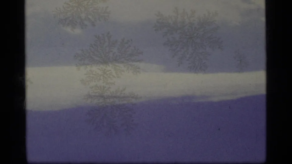 1977 Alaska 8mm frame showing a soft, foggy mountain view with snowfields, purple-blue fading, frame borders, and frost-like artifacts.