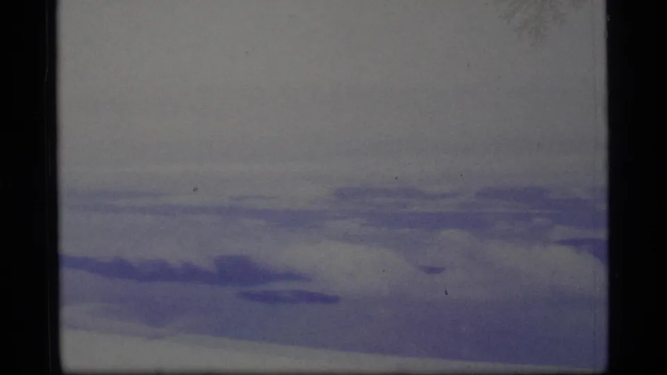 1977 Alaska 8mm frame showing low snow-covered ground, a pale overcast sky, purple color shift, and dark gate edges.