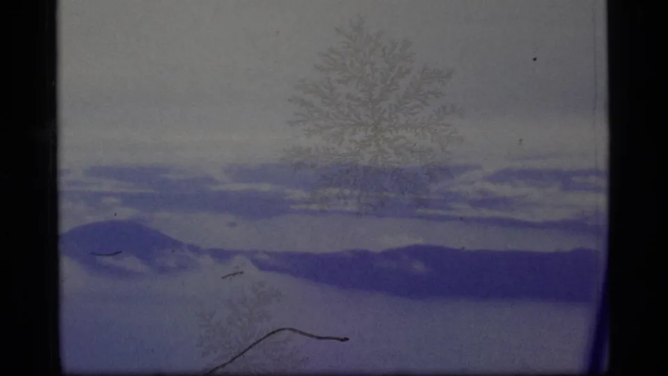 1977 8mm Alaska winter frame showing snow-covered terrain, distant dark ridges, pale sky, and frost-like marks across the film image.