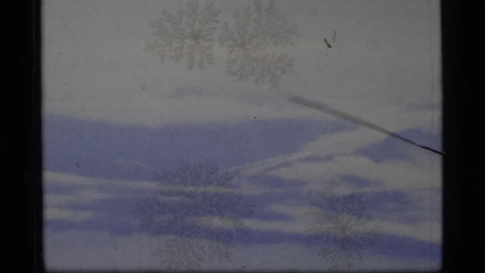 1977 8mm Alaska winter frame with muted snow terrain, blue shadow areas, pale sky, frost-like marks, and a diagonal surface mark.