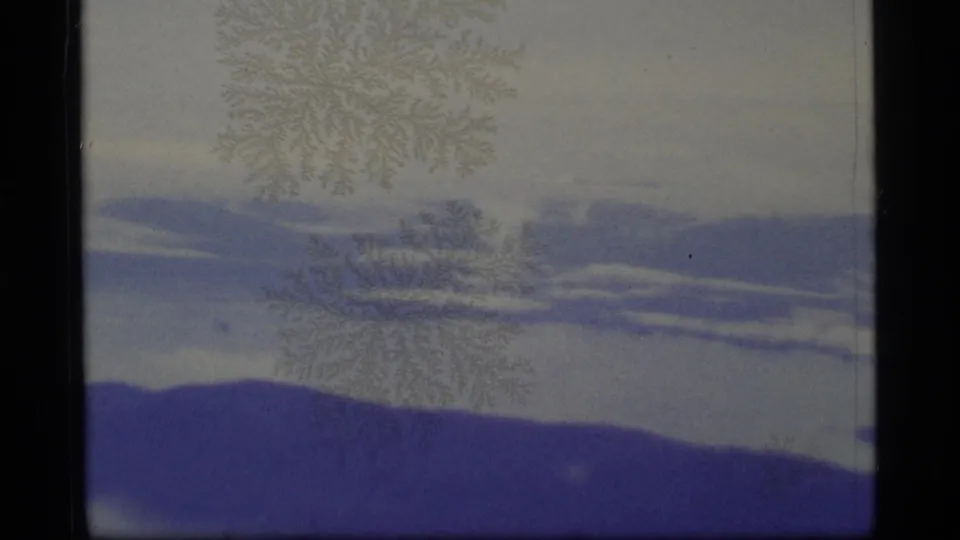 1977 Alaska 8mm frame showing soft blue-gray cloud bands, pale sky, dark film borders, and faint surface patterns.