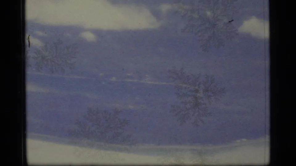 1977 Alaska 8mm frame with blue-gray cloud bands, pale sky, dark borders, grain, and faint surface scratches.