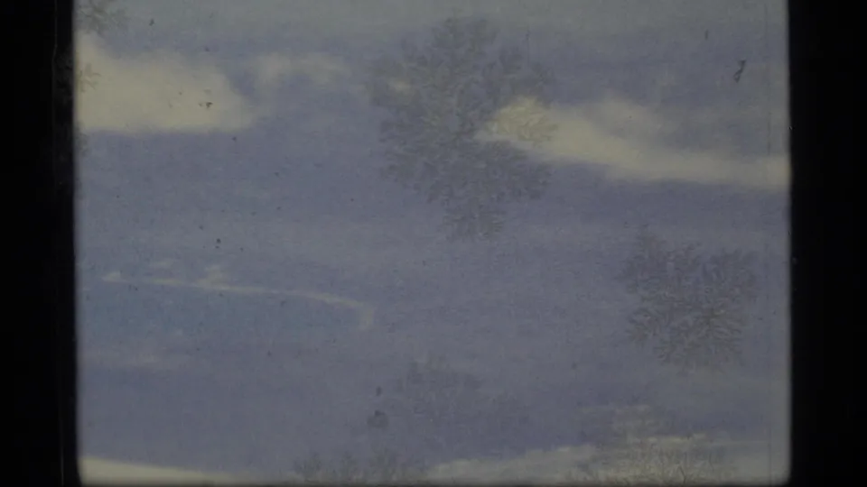 A faded 1977 Alaska Super 8 frame shows dim forest tones and film borders before the totem pole becomes clear.