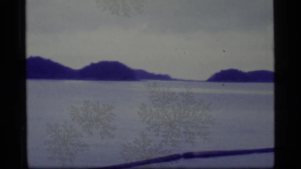 1977 Alaska 8mm frame showing distant island silhouettes beyond a pale frozen or watery expanse with film marks visible.