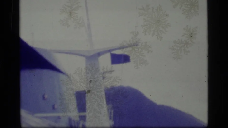1977 Alaska 8mm frame showing a white ship superstructure, dark roofline, small flag-like detail, and soft distant mountain forms.