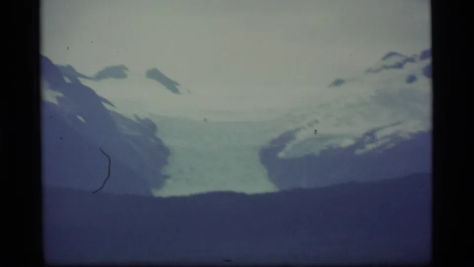 An 8mm Alaska landscape frame shows a glacier and snow-covered mountain forms above a dark ridge and subdued bay tones.