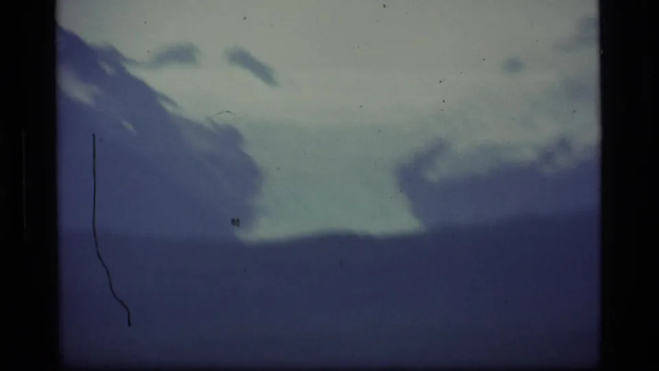 1977 Alaska home-movie frame with snow on a distant mountain slope beyond a dark ridge line.