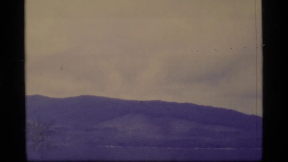 1977 Alaska home-movie frame showing a wide ridgeline and distant mountain forms under a faded sky.