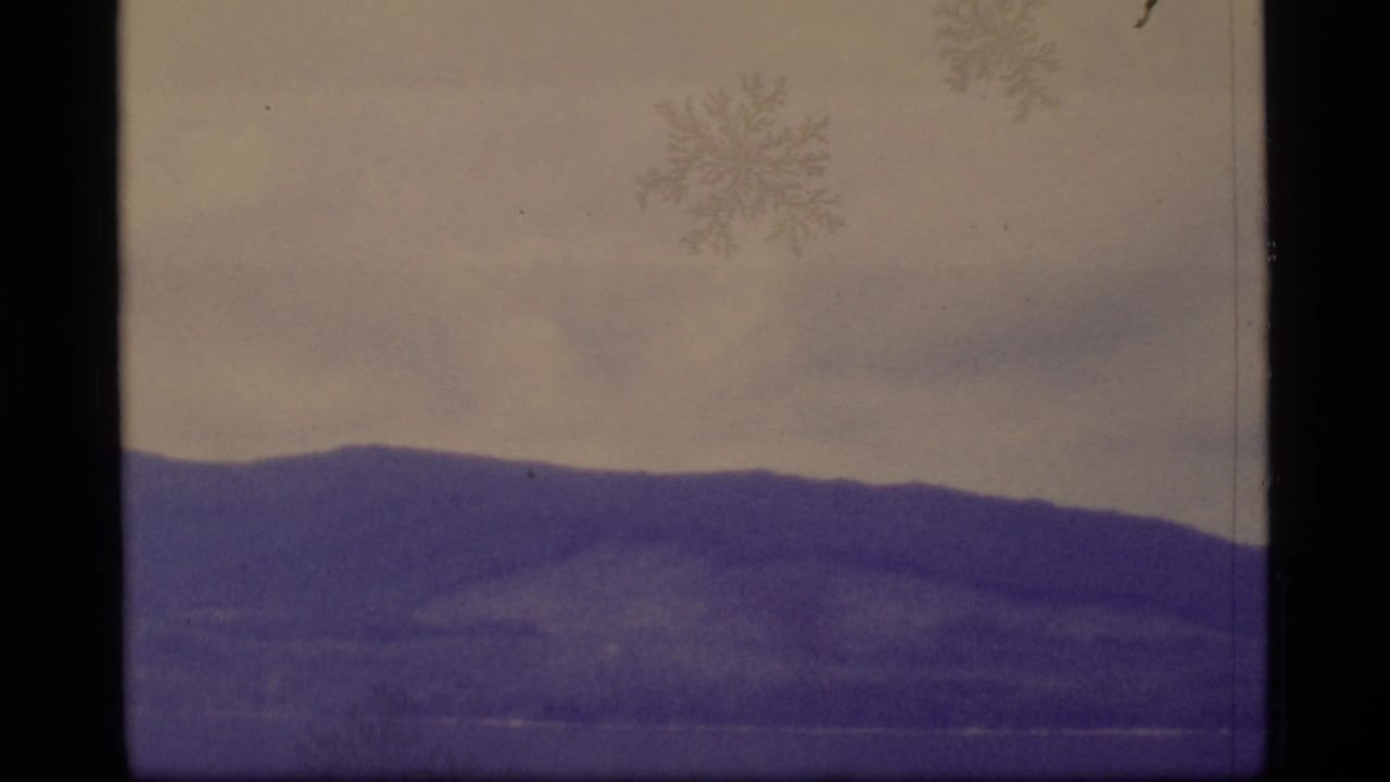1977 Alaska 8mm frame showing a distant mountain ridge beneath a pale sky, with visible film edge and surface artifacts.