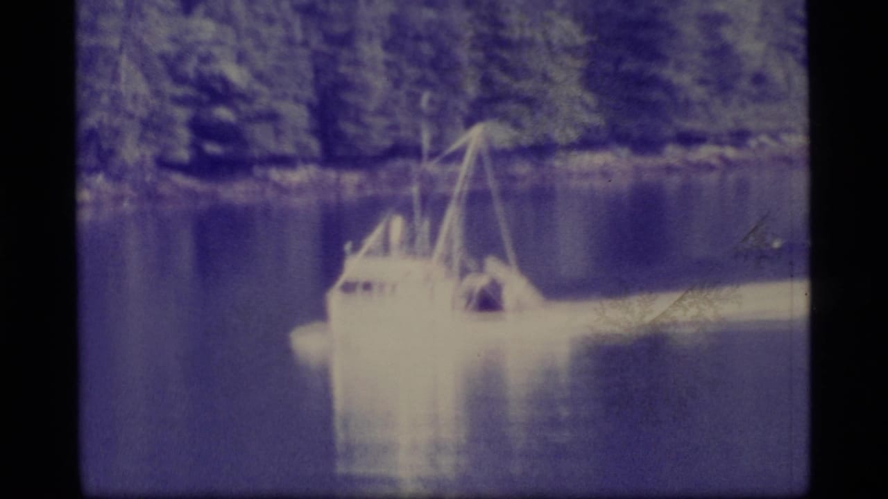 Small cabin boat on a calm lake with evergreen shoreline behind it.